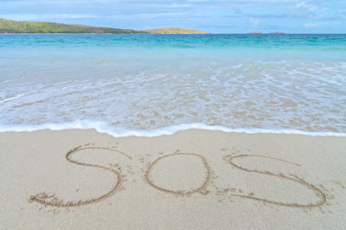 SOS distress sign written in sand of tropical island beach above water