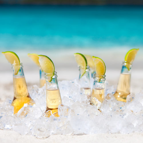seven ice cold beers with limes over ice in sand on the tropical beach in the Caribbean